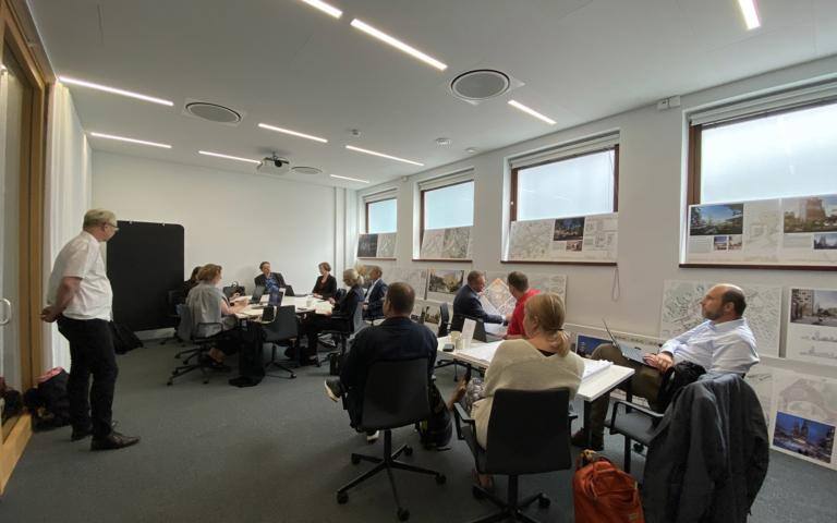 Ihmiset istuvat pöytien ääressä kokoushuoneessa.